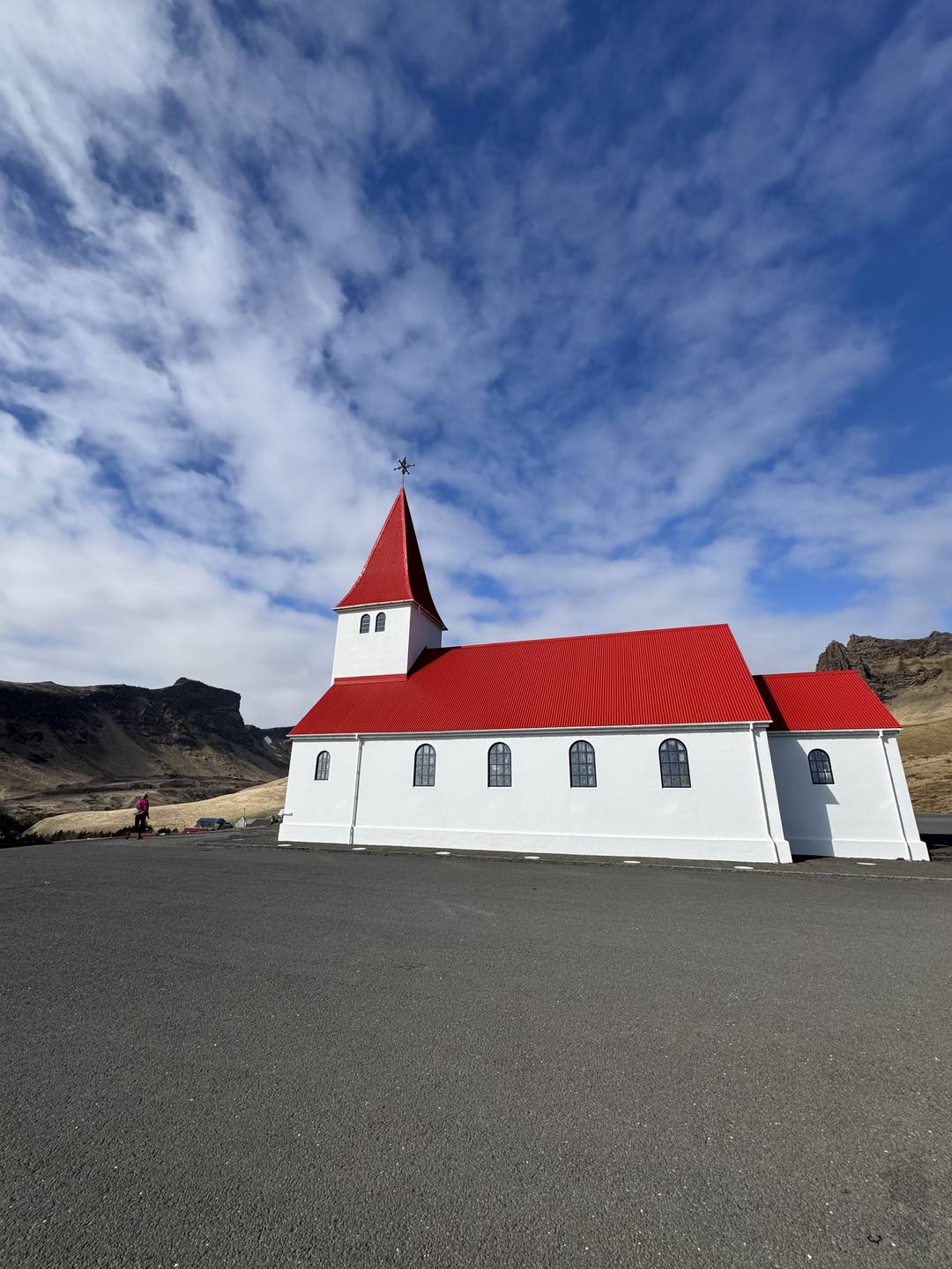 The red-roofed white Víkurkirkja church standing on the green hill above Vík í Mýrdal on Iceland's South Coast